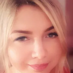 Portret kobiety z blond włosami, patrzącej w obiektyw, z delikatnym uśmiechem i subtelnym makijażem.