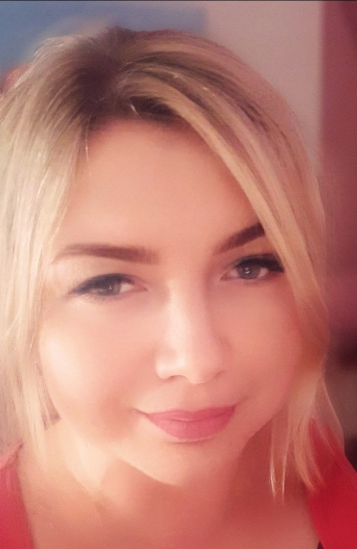 Portret kobiety z blond włosami, patrzącej w obiektyw, z delikatnym uśmiechem i subtelnym makijażem.