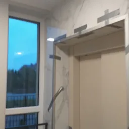 Nowoczesna łazienka z kabiną prysznicową typu walk-in, wykończona płytkami imitującymi marmur, z widocznym oknem i fragmentem balkonu na zewnątrz.