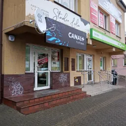 Fasada budynku z szyldami reklamowymi, w tym Canal+ Platforma i Studio Fala, widoczne schody wejściowe i elementy graffiti na ścianie.