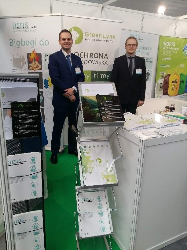 Stoisko targowe firmy Green Lynx z dwoma mężczyznami w garniturach, prezentujące usługi ochrony środowiska i big bagi, z materiałami informacyjnymi i logo firmy.