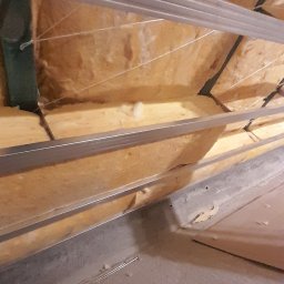 Tomasz skalka - Izolacja termiczna poddasza z widocznymi elementami konstrukcji metalowej i fragmentem sufitu, w trakcie montażu, z perspektywy osoby stojącej na podłodze.