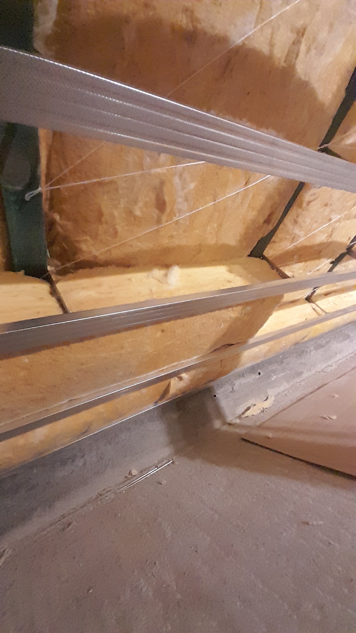 Izolacja termiczna poddasza z widocznymi elementami konstrukcji metalowej i fragmentem sufitu, w trakcie montażu, z perspektywy osoby stojącej na podłodze.