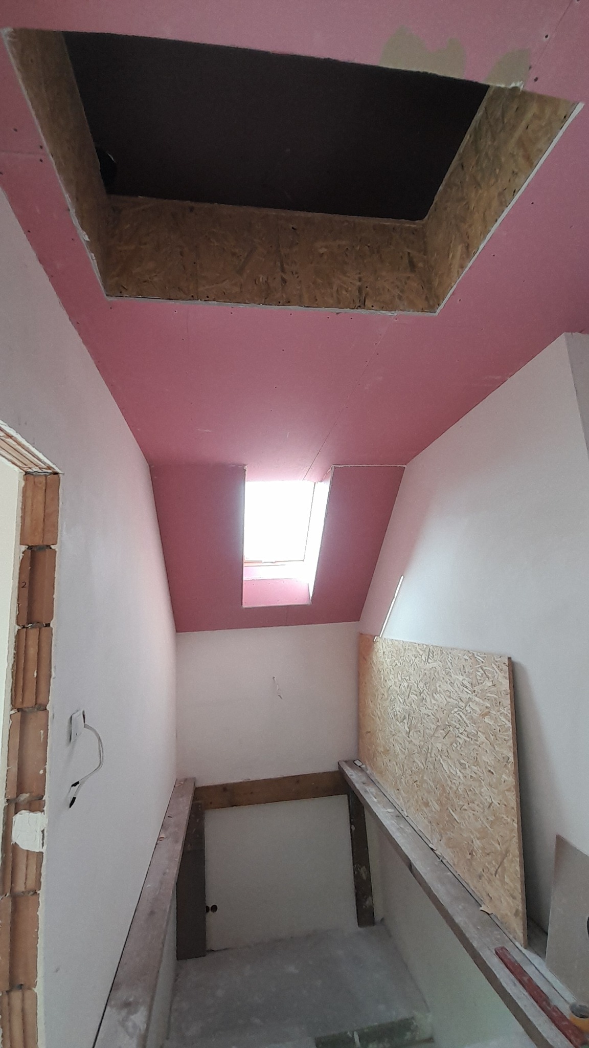 Poddasze w trakcie prac: widoczne płyty kartonowo-gipsowe na skosach, otwór w suficie z obudową z płyty OSB, konstrukcja wsporcza pod podłogę, surowe ściany.