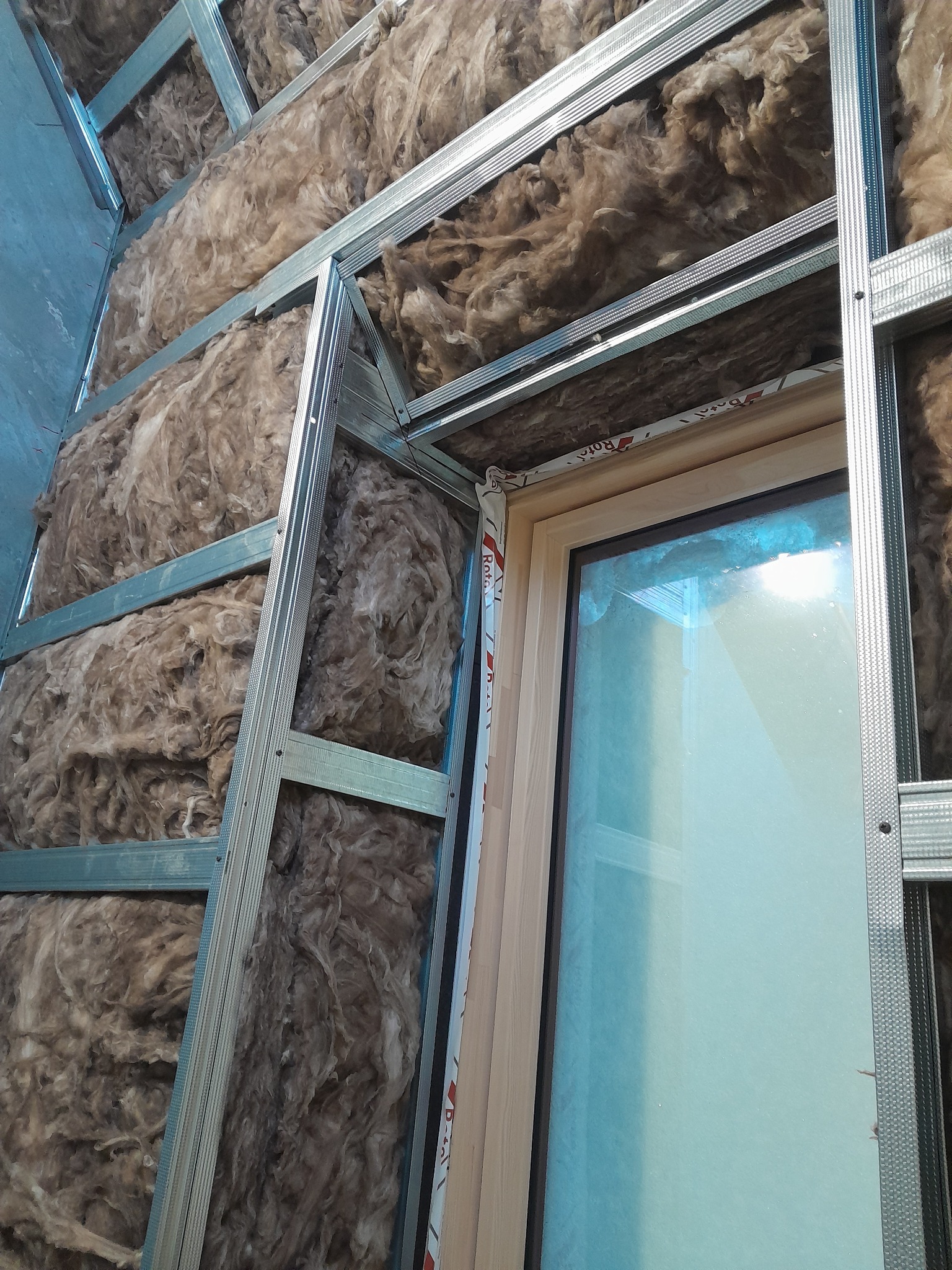 Wypełnienie wełną mineralną w konstrukcji metalowej poddasza, widoczne ramy okienne.