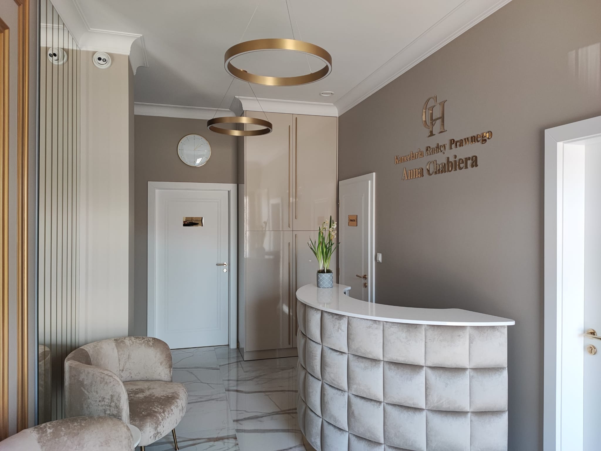 Eleganckie wnętrze kancelarii prawnej z recepcją obitą pikowaną tkaniną, złotymi lampami pierścieniowymi i marmurową podłogą.