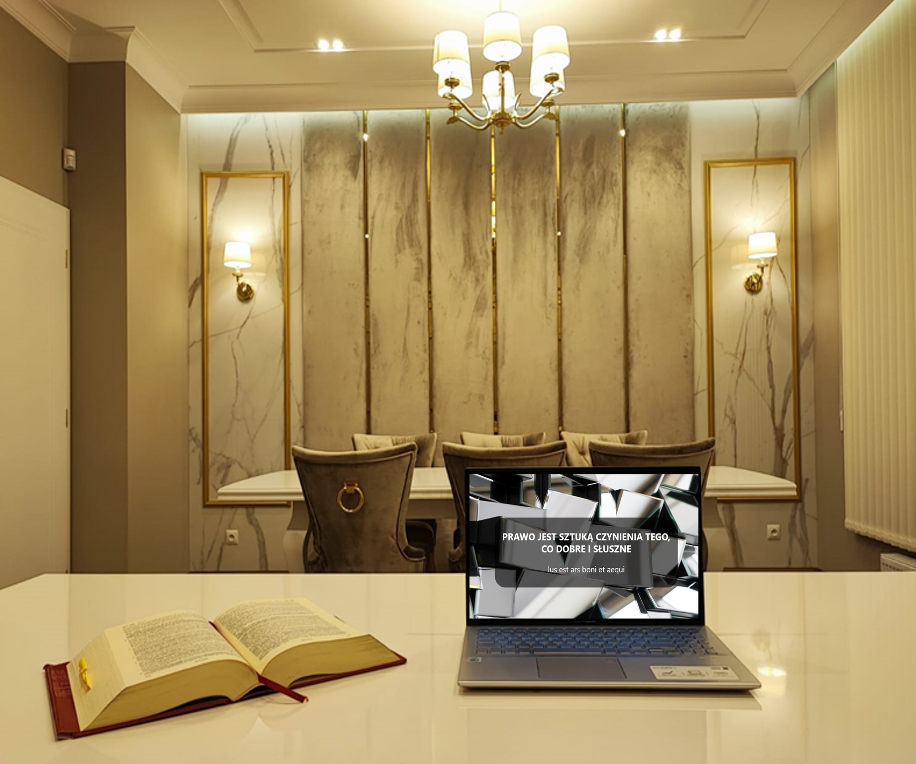 Książka z otwartymi stronami i laptop z napisem 'Prawo jest sztuką czynienia tego, co dobre i słuszne' na błyszczącym białym stole, w tle luksusowo urządzone wnętrze z marmurowymi panelami...