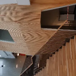 Nowoczesne schody drewniane z metalową balustradą, w budynku z drewnianą boazerią i oknami dachowymi, widoczny sprzęt budowlany.