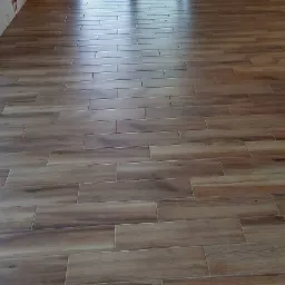 Ułożona podłużna, brązowa terakota imitująca drewno na podłodze, widoczne fugi i odbicie światła od okna.