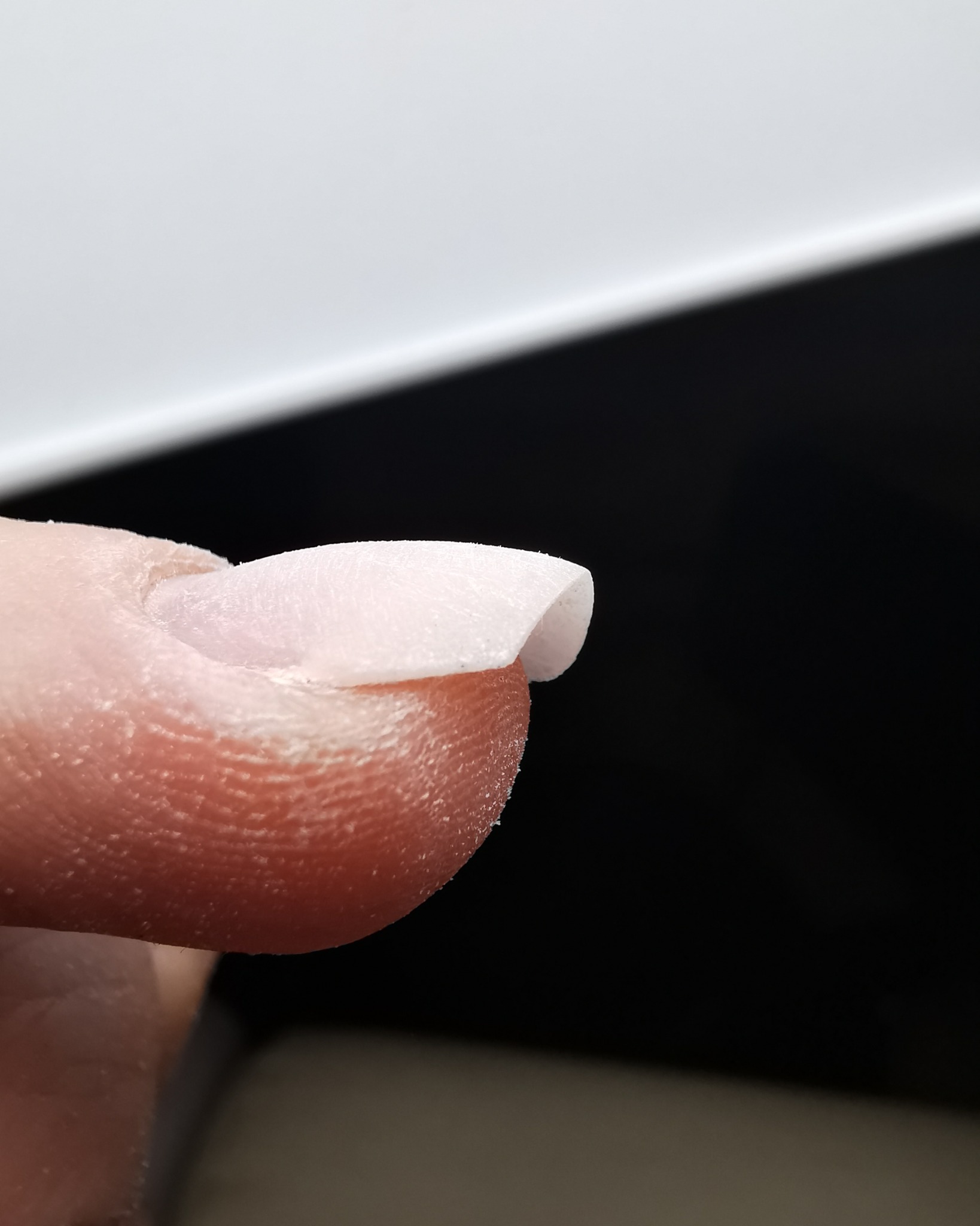 Makro zbliżenie na palec z nałożoną warstwą akrylu lub żelu na paznokciu, przygotowanego do dalszej obróbki pilnikiem.