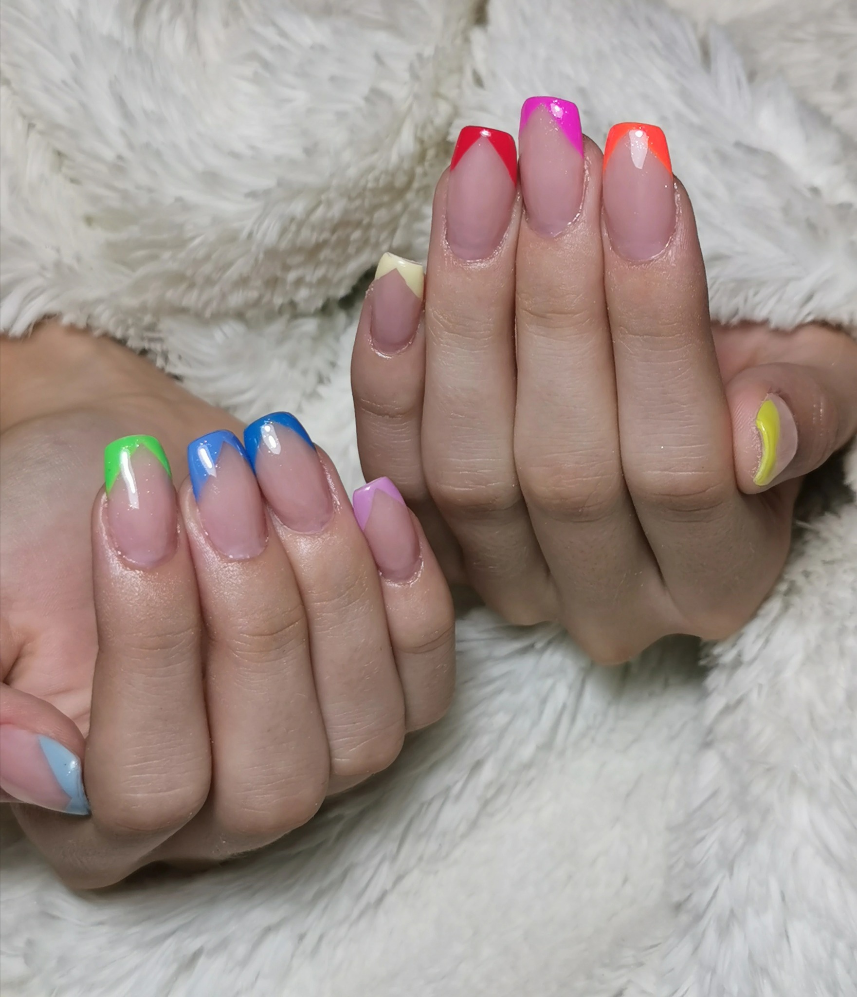 Dłonie z pomalowanymi paznokciami w stylu french manicure, każdy paznokieć z końcówką w innym, jaskrawym kolorze (różowy, czerwony, pomarańczowy, żółty, zielony, niebieski, fioletowy, błękitny...