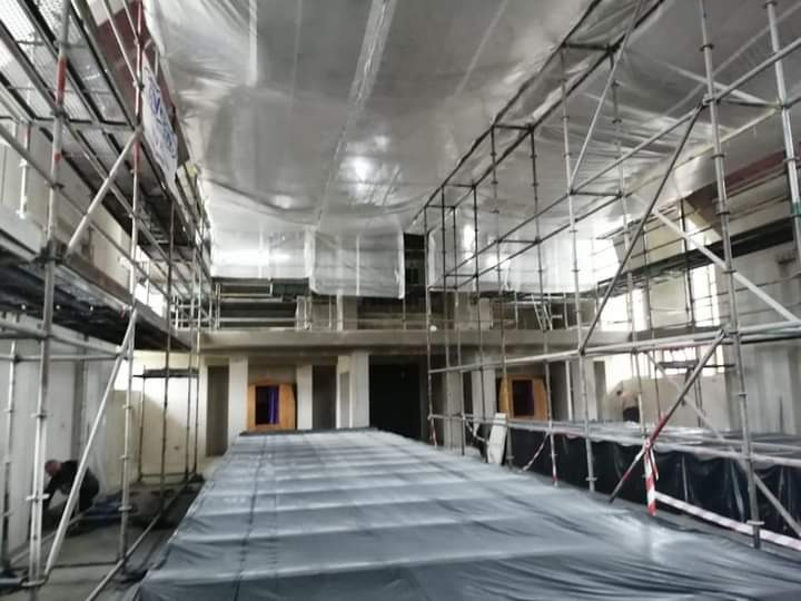 Wnętrze budynku w trakcie prac przygotowawczych do nakładania tynków maszynowych, zabezpieczone folią ochronną, widoczne rusztowania i pracownik przy ścianie.