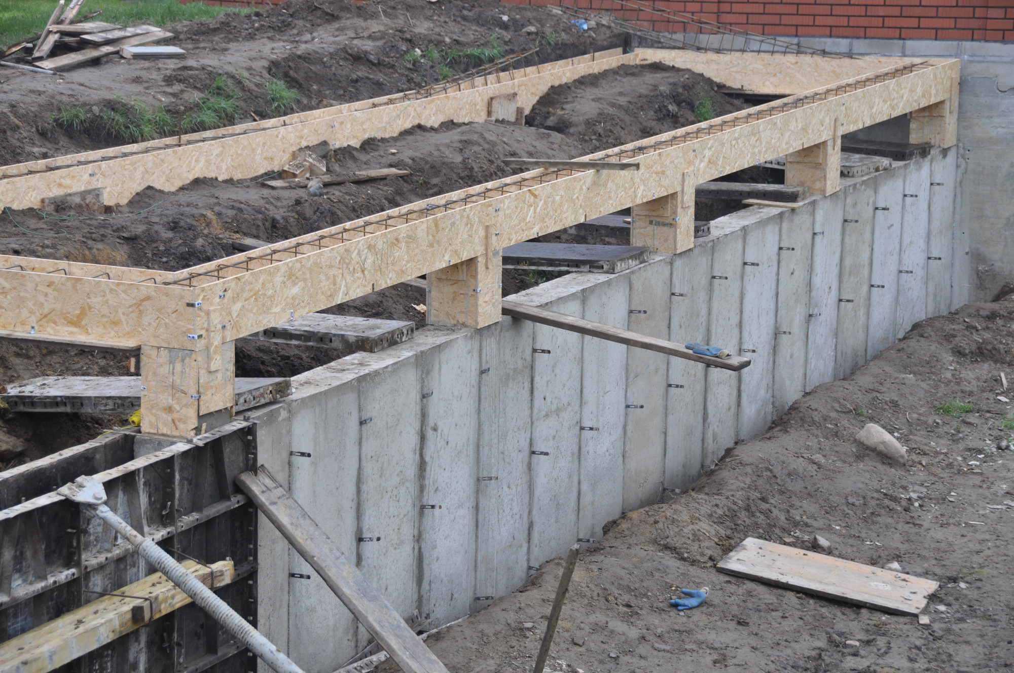 Betonowy fundament domu w trakcie budowy z widocznym szalunkiem z płyty OSB i zbrojeniem, ziemia wokół fundamentu.
