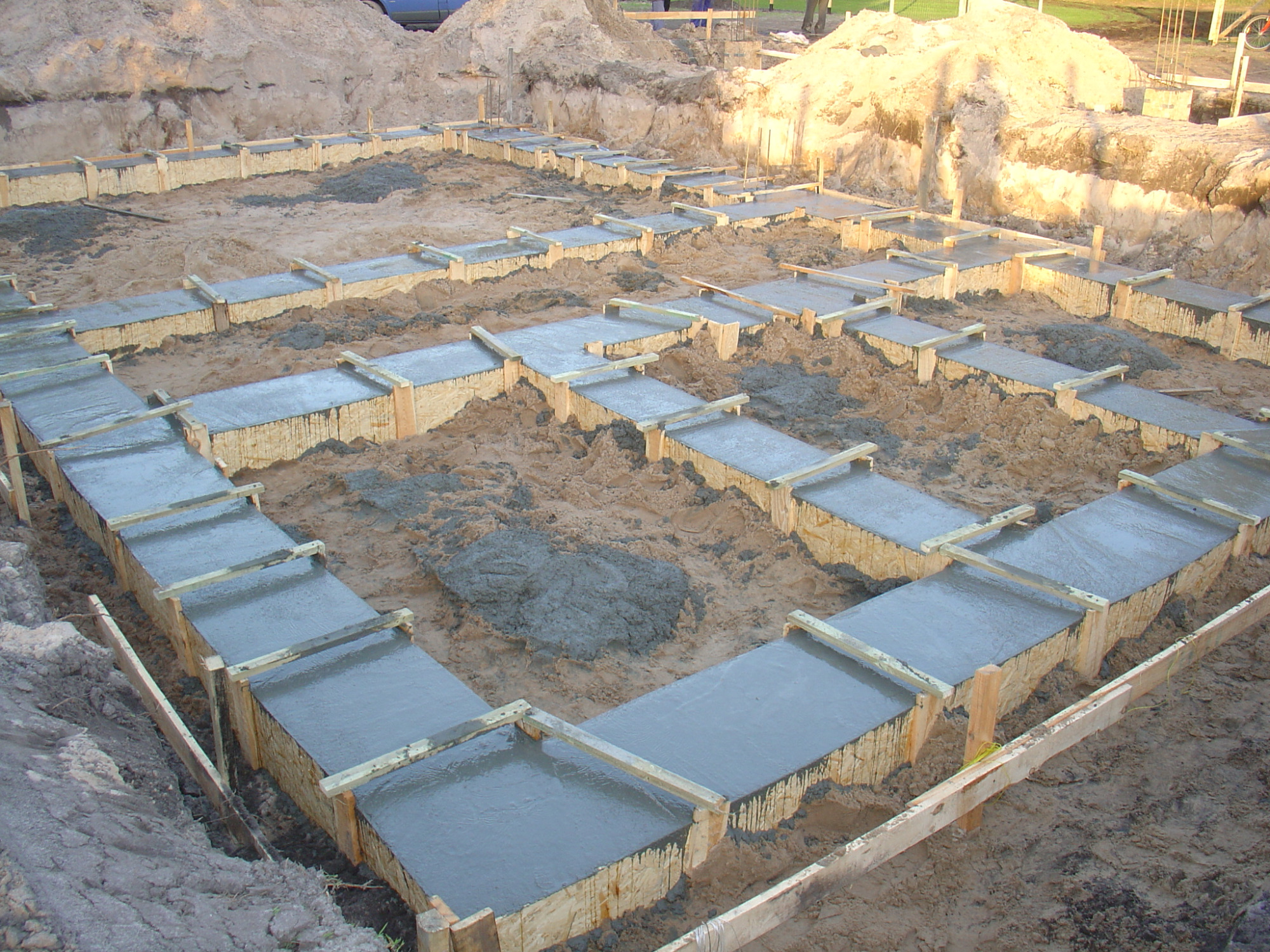 Zalane betonem szalunki fundamentowe w wykopie, widoczne drewniane deski i mokry beton, przygotowanie do wylania fundamentów domu.