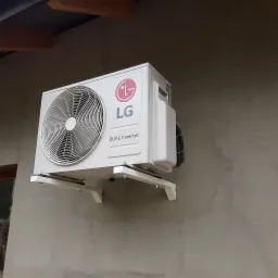 Zewnętrzna jednostka klimatyzacji LG Dual Inverter zamontowana na wspornikach na szarej, surowej ścianie budynku z widocznymi śladami tynku.