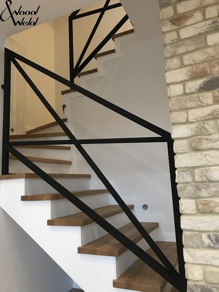 Nowoczesne schody z drewnianymi stopniami i czarną, geometryczną balustradą metalową, widok z dołu, ściana wykończona imitacją cegły.