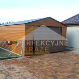 M-Trans - Gotowy, brązowy garaż blaszany z bramą segmentową, widoczny z zewnątrz na posesji z kostką brukową, obok samochód i suszarka na pranie.