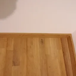 Fragment drewnianej boazerii na ścianie, z widocznym gniazdkiem elektrycznym po prawej stronie i delikatnym cieniem na górze.