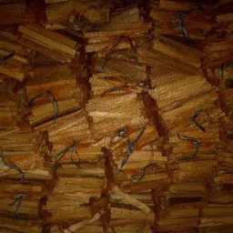 Stos worków siatkowych wypełnionych pociętymi kawałkami drewna, związanych niebieskim sznurkiem, tworzących uporządkowany, ale surowy magazyn opału.