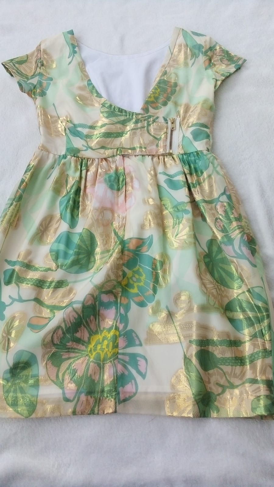 Sukienka damska z krótkim rękawem, w pastelowych odcieniach zieleni, różu i złota, z motywem kwiatowym i ozdobnym zamkiem błyskawicznym w pasie, leżąca na białym tle.