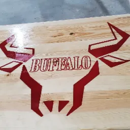 Lakierowany blat z jasnego drewna z wygrawerowanym, czerwonym motywem graficznym głowy bizona i napisem 'BUFFALO'.