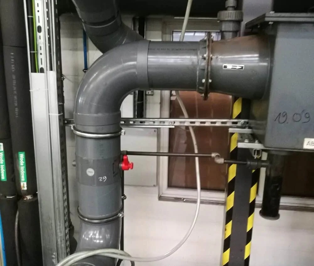 Szare rury przemysłowe z zaworem w instalacji wentylacyjnej lub klimatyzacyjnej, widok z wnętrza budynku w Warszawie.