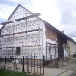 Marcin Rydzik Usługi Ogólnobudowlane - Dom w trakcie ocieplania, styropian przyklejony do elewacji, rusztowania ustawione wzdłuż ściany, fragment ściany z cegły nieocieplony.