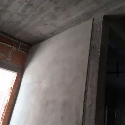 Świeżo otynkowana ściana wewnętrzna z widoczną surową konstrukcją stropu i fragmentem otworu drzwiowego w stanie deweloperskim.