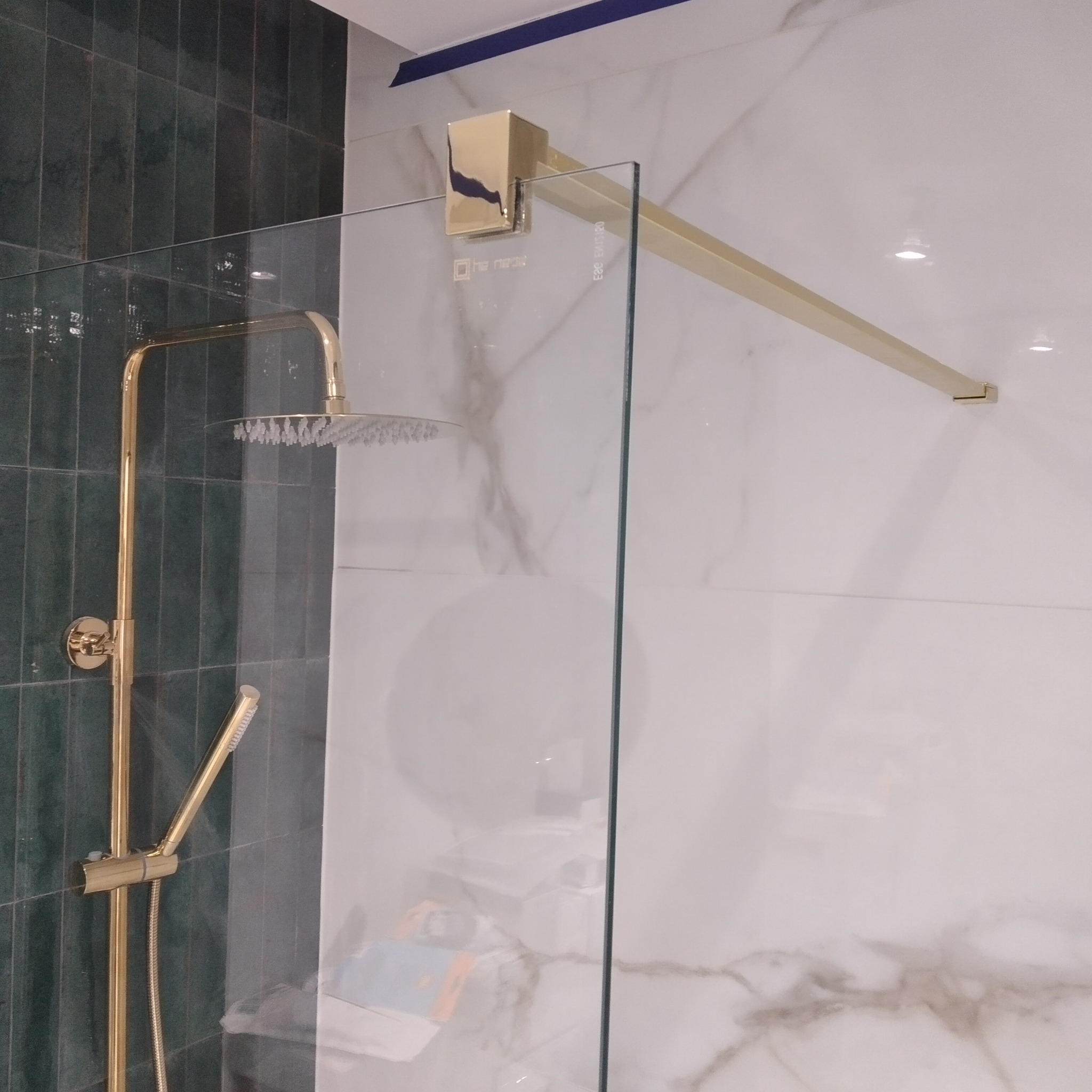 Kabina prysznicowa ze złotą armaturą na tle zielonych i marmurowych płytek.