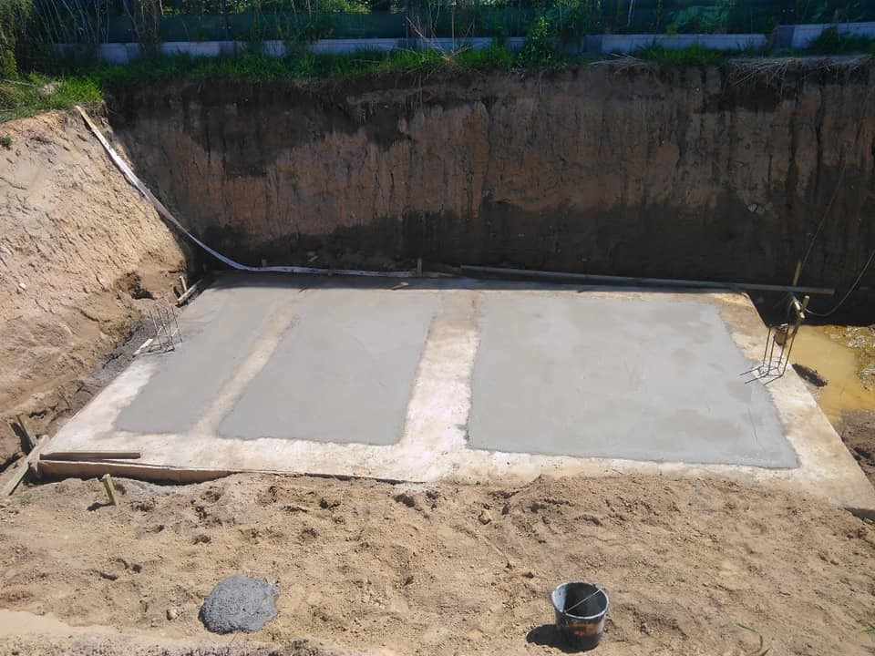 Wylany betonowy fundament w wykopie, widoczne zbrojenia i błoto, teren budowy w trakcie prac ziemnych.
