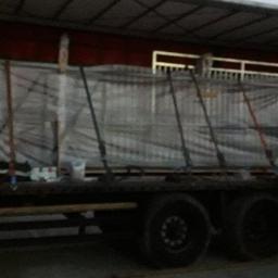 SDI Sp. z o.o. - Załadunek konstrukcji stalowej na naczepę ciężarówki, zabezpieczonej pasami transportowymi i folią stretch, w tle widoczny pracownik w odblaskowej kamizelce.