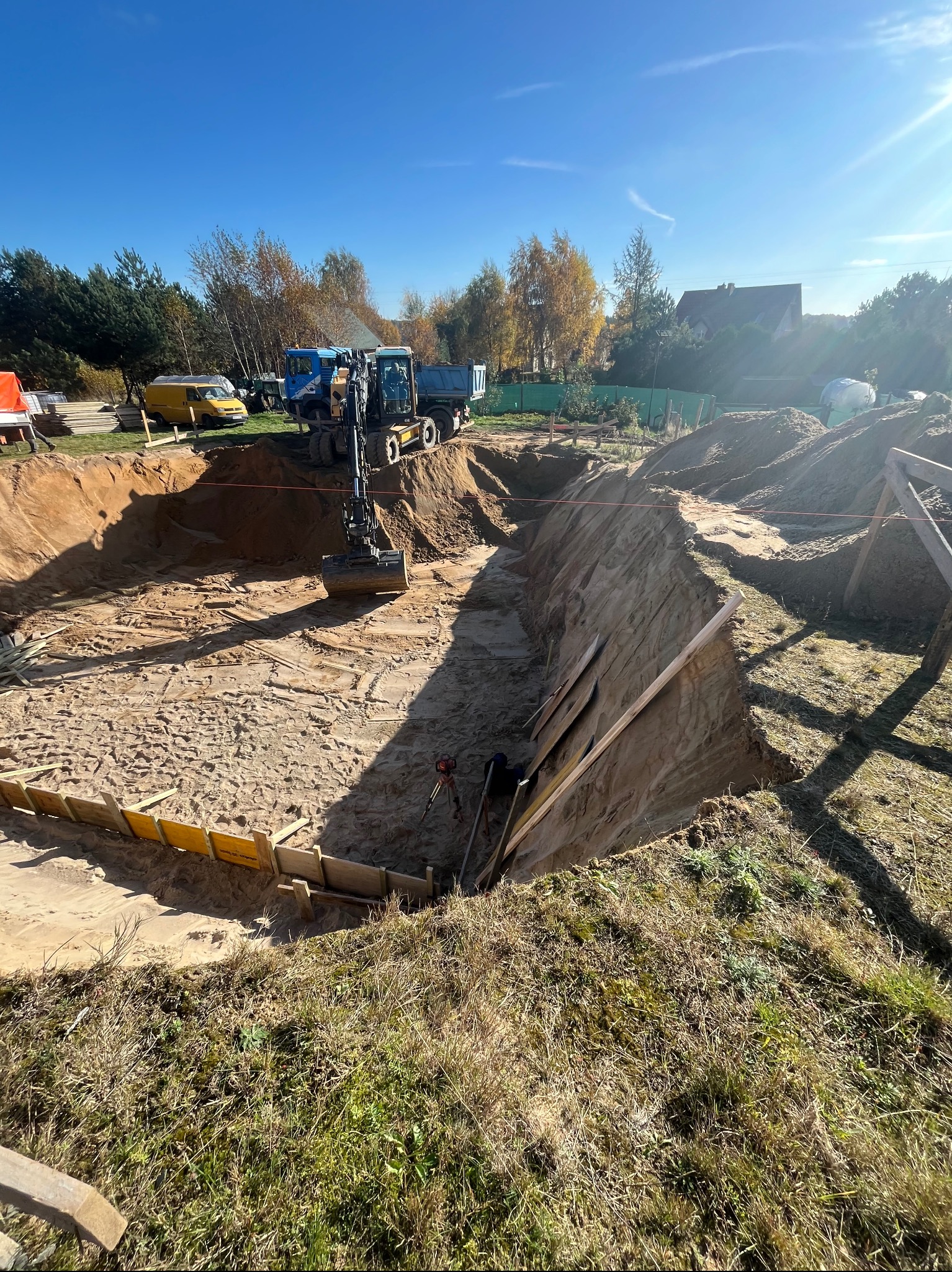 Wykop pod fundamenty z żółtym szalunkiem w Kielnie, wykonany koparką, z widocznym transportem ziemi i przygotowanym terenem pod budowę.