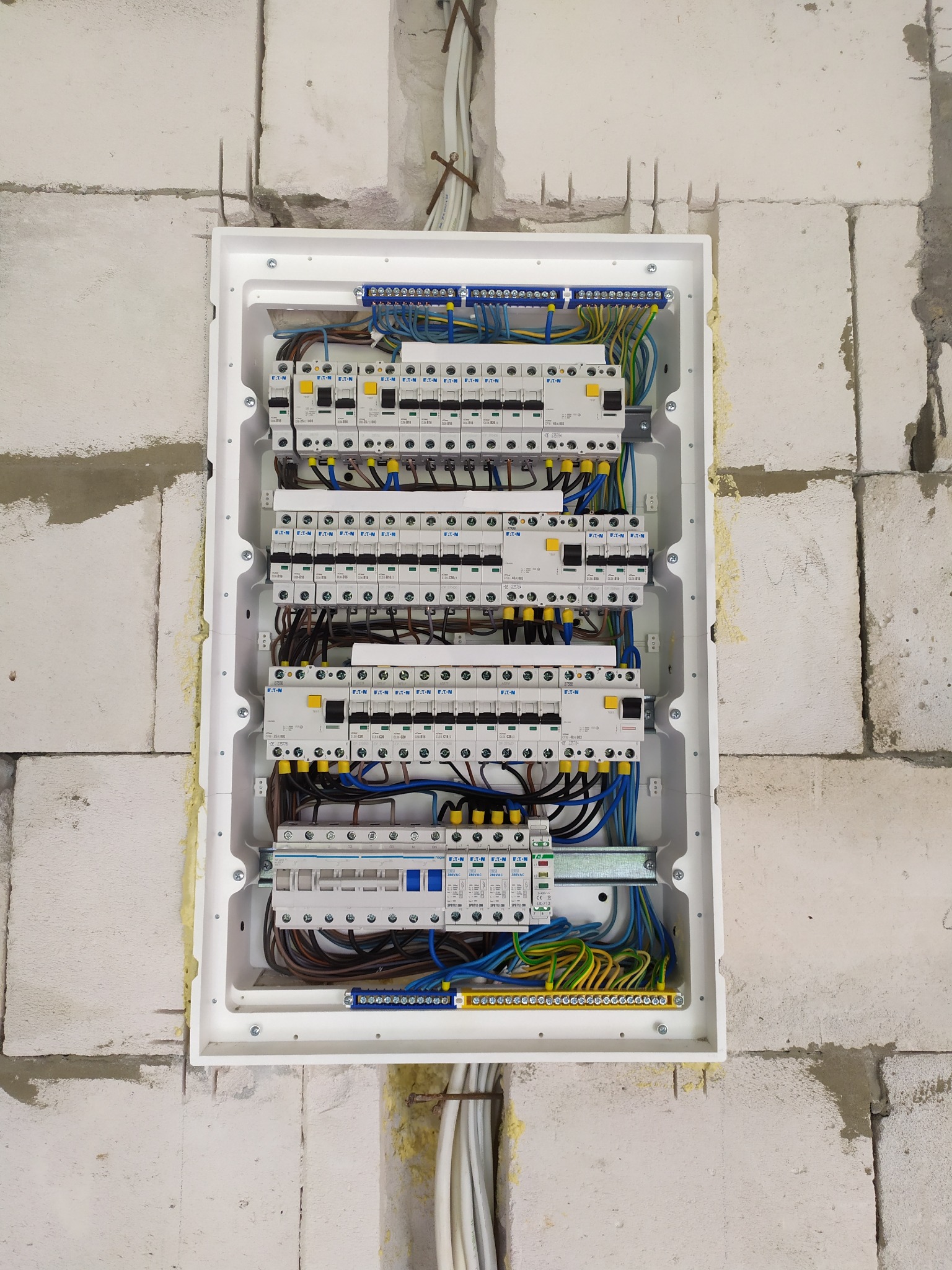 Rozdzielnica elektryczna Eaton w białej obudowie, zamontowana w surowej ścianie z betonu komórkowego, widoczne przewody elektryczne i bezpieczniki.