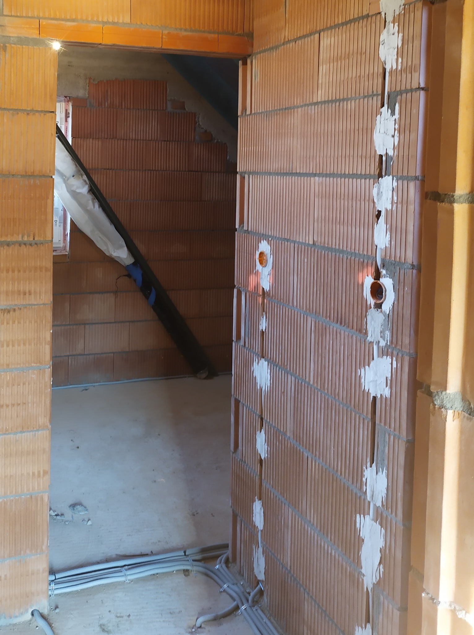 Surowy stan instalacji elektrycznej w nowo budowanym domu w Zawoi, widoczne kable w peszlach prowadzone po podłodze i pionowe bruzdy w murze wypełnione gipsem, z puszkami pod gniazdka.