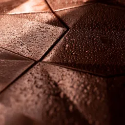 Metalowa powierzchnia pokryta kroplami wody, ułożona z trójkątnych elementów w odcieniach brązu, z bliska i pod kątem.