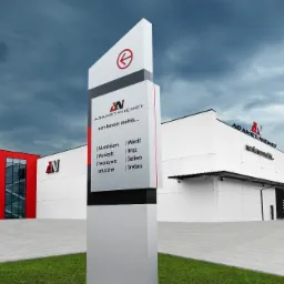 Zewnętrzny widok budynku firmy Adamet Niemet z tablicą informacyjną prezentującą logo i ofertę metali nieżelaznych: aluminium, miedź, mosiądz, brąz, żeliwo, tworzywa sztuczne i srebro.