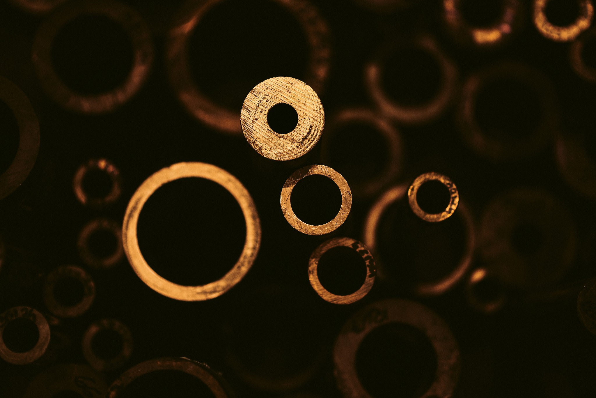 Makro ujęcie miedzianych pierścieni o różnej grubości i średnicy, z widoczną fakturą obróbki metalu i ciepłym oświetleniem.