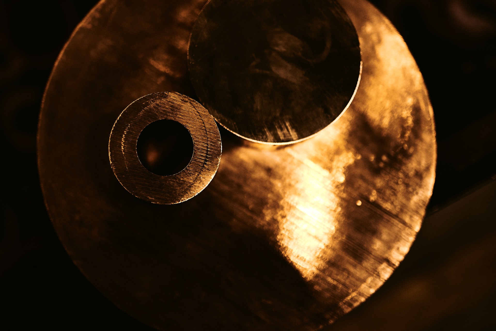 Dwa okrągłe elementy metalowe z widocznymi śladami obróbki skrawaniem, oświetlone ciepłym światłem na ciemnym tle.
