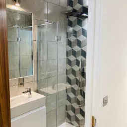 Nowoczesna łazienka z kabiną prysznicową, umywalką nablatową i geometrycznymi płytkami w strefie prysznica.