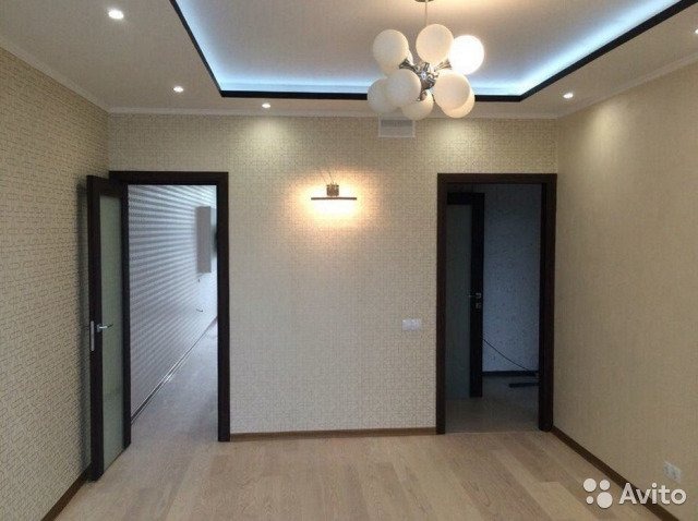 Jasne wnętrze pokoju po remoncie z drewnianą podłogą, dwojgiem ciemnych drzwi i nowoczesnym oświetleniem sufitowym