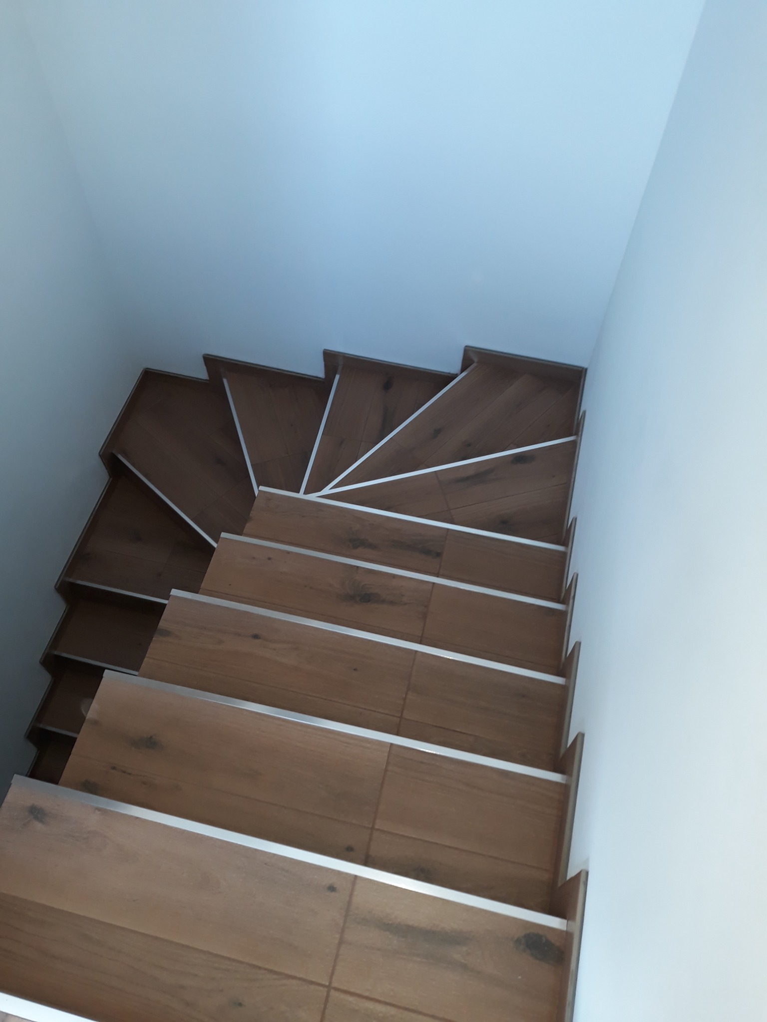 Klatka schodowa wykończona płytkami imitującymi drewno z aluminiowymi listwami krawędziowymi, widok z góry.