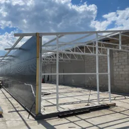 Konstrukcja hali w trakcie budowy: stalowy szkielet z zamontowanymi płytami warstwowymi, widoczne elementy mocujące. Słoneczny dzień, błękitne niebo z chmurami.