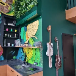 Nowoczesna kuchnia z drewnianymi szafkami, czarnym blatem i kolorowym muralem na ścianie, uzupełniona o wiszące gitary.