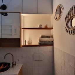 Katarzyna Kuczyńska Projektowanie Wnętrz - Nowoczesna łazienka z geometryczną podłogą, drewnianą szafką pod umywalką z marmurowym blatem, toaletą, półką z podświetleniem LED i dekoracyjnymi lustrami w kształcie oka.