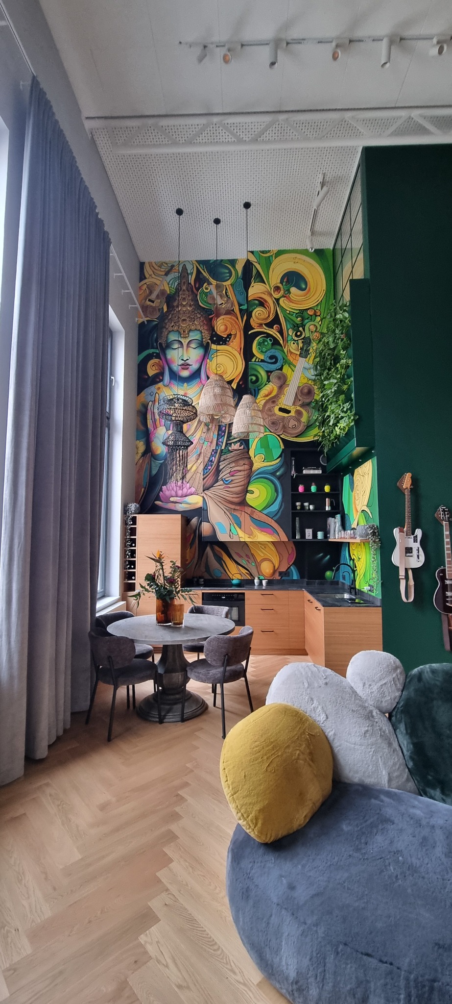 Nowoczesne wnętrze z muralem Buddy, drewnianymi meblami kuchennymi, okrągłym stołem jadalnym i designerskimi poduszkami na sofie.