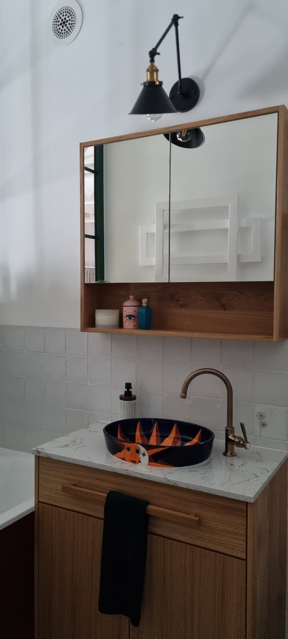 Umywalka nablatowa w kolorze granatowym z motywem słońca, bateria w kolorze mosiądzu, szafka pod umywalkę z drewnianymi frontami, lustro w drewnianej ramie z półką, oświetlenie punktowe w stylu retro.