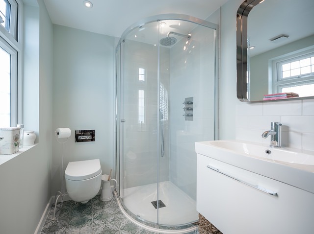 Jasna łazienka po remoncie z kabiną prysznicową typu walk-in, białą umywalką z szafką, wiszącą toaletą i wzorzystą podłogą w odcieniach zieleni i błękitu.