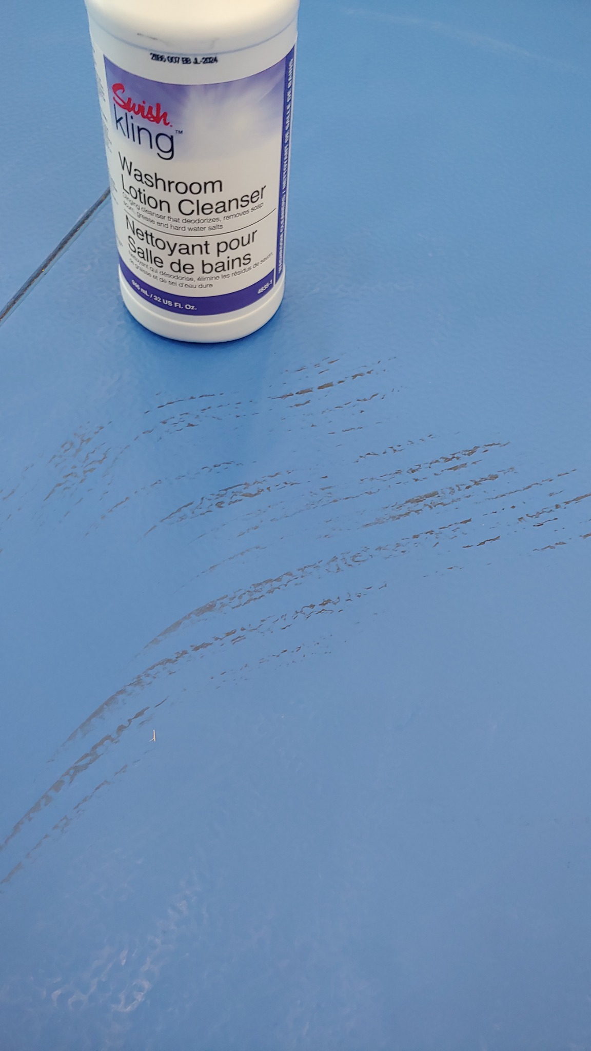 Butelka środka czyszczącego Swish Kling Washroom Lotion Cleanser na niebieskiej, lekko zabrudzonej powierzchni podłogi.