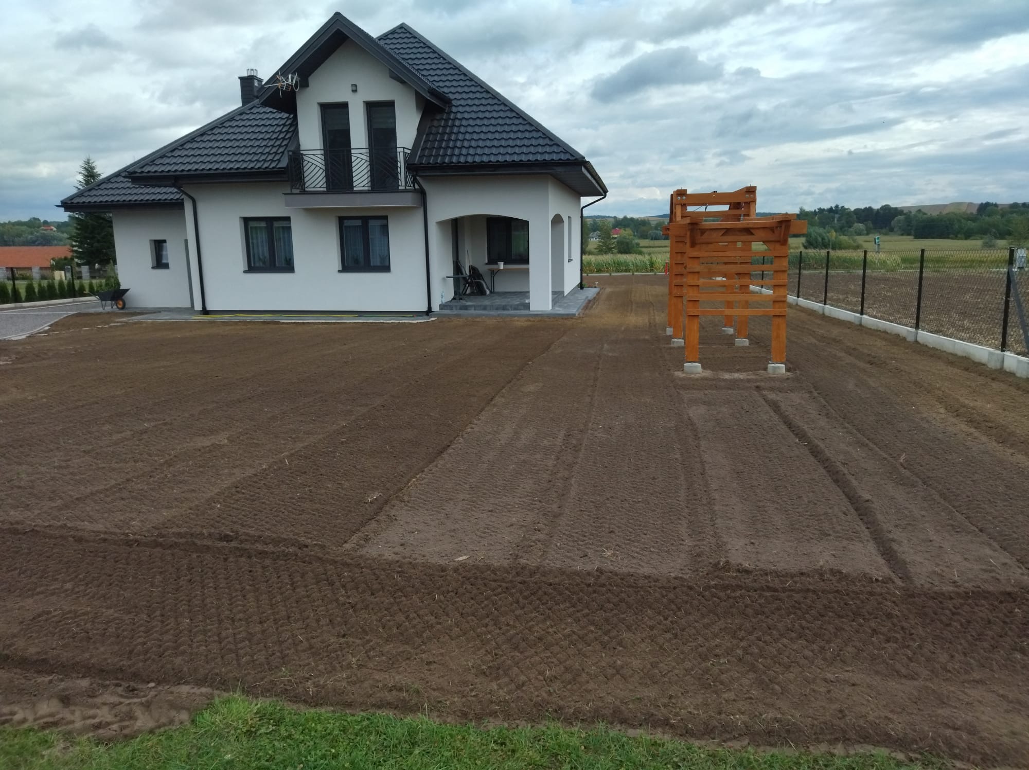 Przygotowany teren pod trawnik z rolki w Kańczudze, widoczne ślady po maszynach i konstrukcja drewniana w tle.