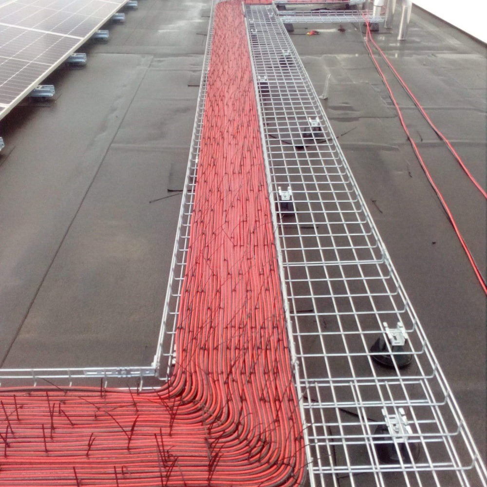 Czerwone kable ułożone w metalowych korytach na dachu w Malmö, obok paneli słonecznych.